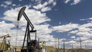 Oil pumpjack operating in a wide-open oil field under a blue sky with scattered clouds