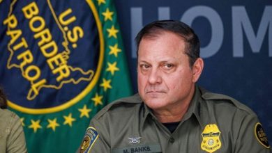 Border Patrol agent M. Banks in uniform at a press conference, with agency patches and a seals backdrop behind him.