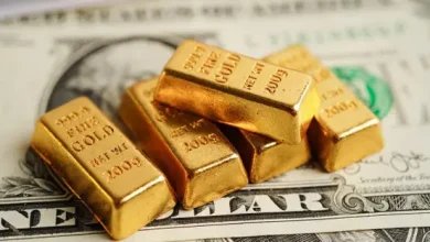 Pile of gold bullion bars resting on a US dollar bill, bars stamped 1 oz fine gold with year marks visible.