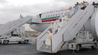 56 | MCG24 | موقع إلكتروني مغربي شامل متجدد على مدار الساعة People in white traditional robes boarding a Boeing aircraft via mobile stairs at a tarmac; plane has a green-red-white stripe along the fuselage.
