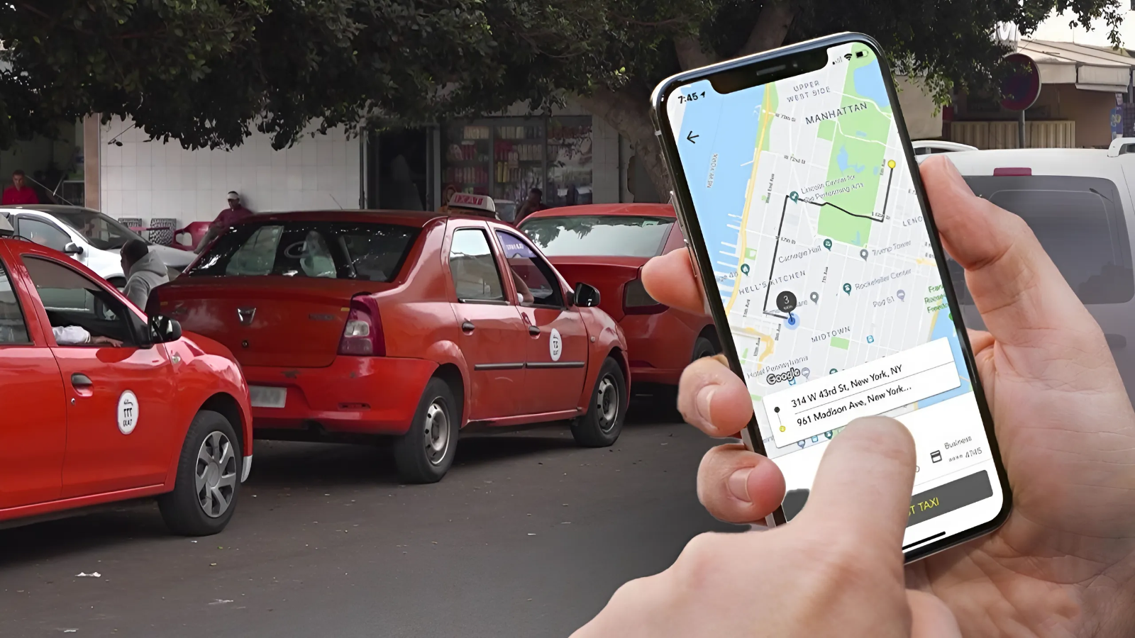 Close-up of a hand holding a smartphone showing a ride-hailing map, with red taxis lined up on the street in the background.