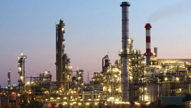 Industrial refinery complex with tall smokestacks and glowing lights at dusk.