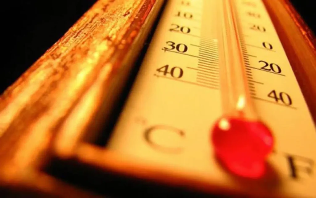 Close-up of a thermometer with red mercury near 40°C on a yellow scale under warm light.