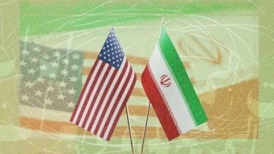 Two small national flags, United States and Iran, planted upright on a green abstract background.