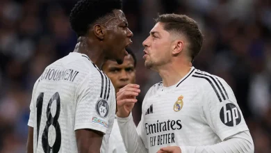 Two Real Madrid players in white jerseys confront each other on the field, one with the number 18 on his back shouting toward the other.