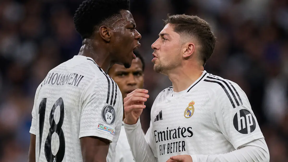 Two Real Madrid players in white jerseys confront each other on the field, one with the number 18 on his back shouting toward the other.