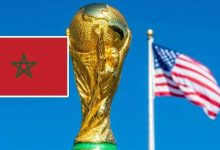 FIFA World Cup trophy with a Moroccan flag in the foreground and an American flag waving in the blue sky behind.