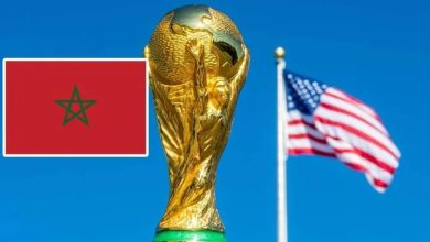 69deae65ee7fa8c49f450813_default | MCG24 | موقع إلكتروني مغربي شامل متجدد على مدار الساعة FIFA World Cup trophy with a Moroccan flag in the foreground and an American flag waving in the blue sky behind.