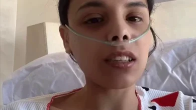 Woman in a hospital bed speaking to the camera, wearing a nasal oxygen cannula.