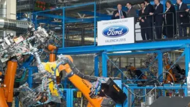 Ford Valencia 2015 event: executives on a viewing balcony overlook a robotic assembly line with orange robotic arms in a car production plant.