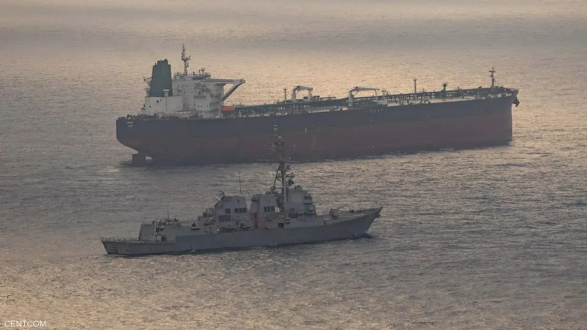 Two ships at sea during sunset: a large tanker in the background and a gray naval vessel in the foreground