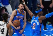 8739649_1779340543 | MCG24 | موقع إلكتروني مغربي شامل متجدد على مدار الساعة Thunder players in blue uniforms share an intense moment on the court; one guards the ball and shouts while a teammate raises an arm, opposing white #24 watches.