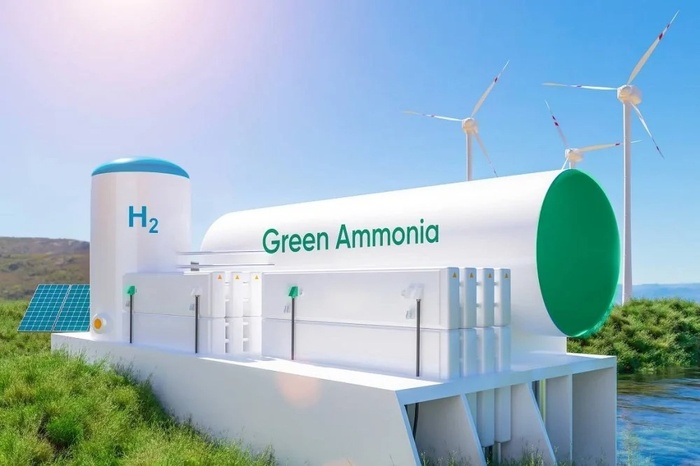 Large white storage tank labeled "Green Ammonia" with an "H2" marker, set in a grassy area with wind turbines in the background and solar panels nearby.