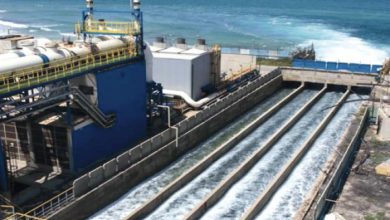 Industrial water treatment plant with open troughs carrying flowing water, adjacent to the ocean sea breeze visible nearby.