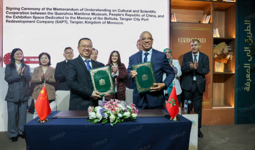 Officials sign a Memorandum of Understanding on cultural and scientific cooperation, standing behind a table with green documents and flags on display.
