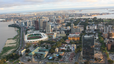 Aerial view of a coastal city with a large oval stadium, high-rise buildings, and a riverfront.