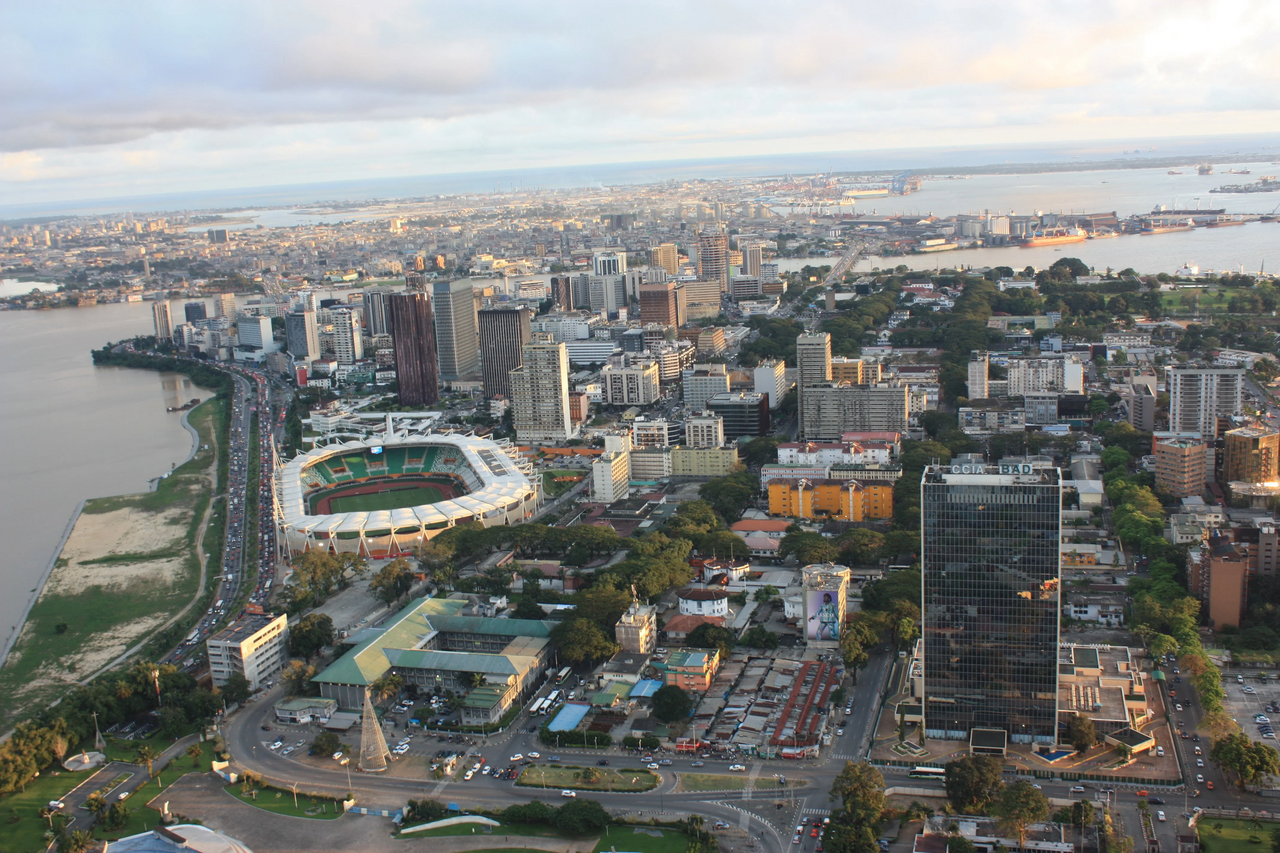 Aerial view of a coastal city with a large oval stadium, high-rise buildings, and a riverfront.