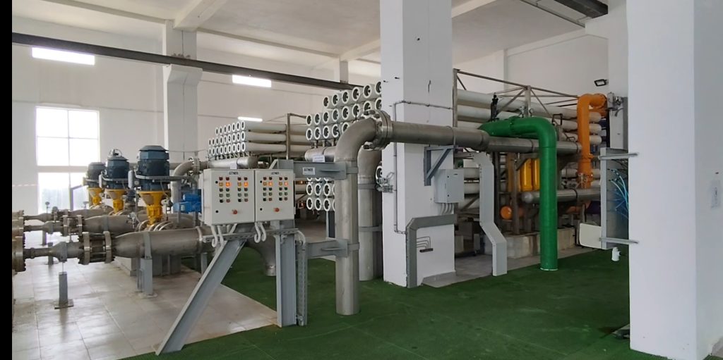Industrial processing room with large stainless steel pipes, valves, and control panels.