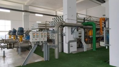 Industrial processing room with large stainless steel pipes, valves, and control panels.
