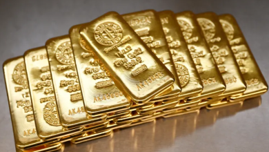 Stack of gold bars arranged in a neat row on a reflective surface, gleaming bullion.