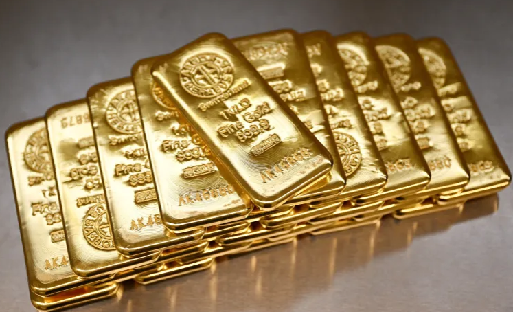Stack of gold bars arranged in a neat row on a reflective surface, gleaming bullion.