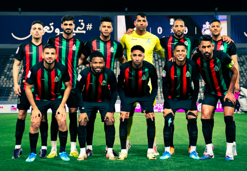 Eleven soccer players in black jerseys with green and red stripes pose for a team photo on a soccer field, with the goalkeeper in yellow in the back row.