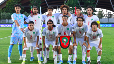 Capture décran 2026-05-21 à 182111 | MCG24 | موقع إلكتروني مغربي شامل متجدد على مدار الساعة Eleven soccer players in white uniforms pose for a group photo on a soccer field, with a shield emblem held by the center player in front.