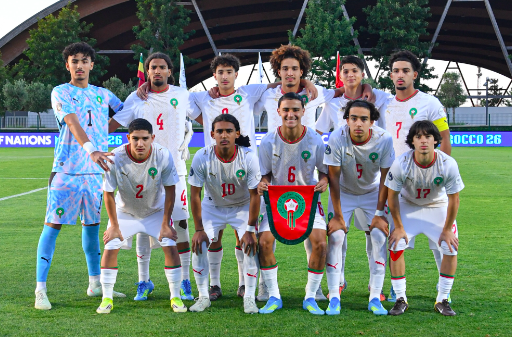 Capture décran 2026-05-21 à 182111 | MCG24 | موقع إلكتروني مغربي شامل متجدد على مدار الساعة Eleven soccer players in white uniforms pose for a group photo on a soccer field, with a shield emblem held by the center player in front.