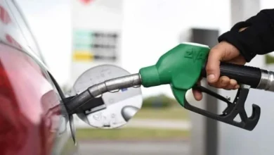 Person pumping gasoline into a red car using a green fuel nozzle at a gas station