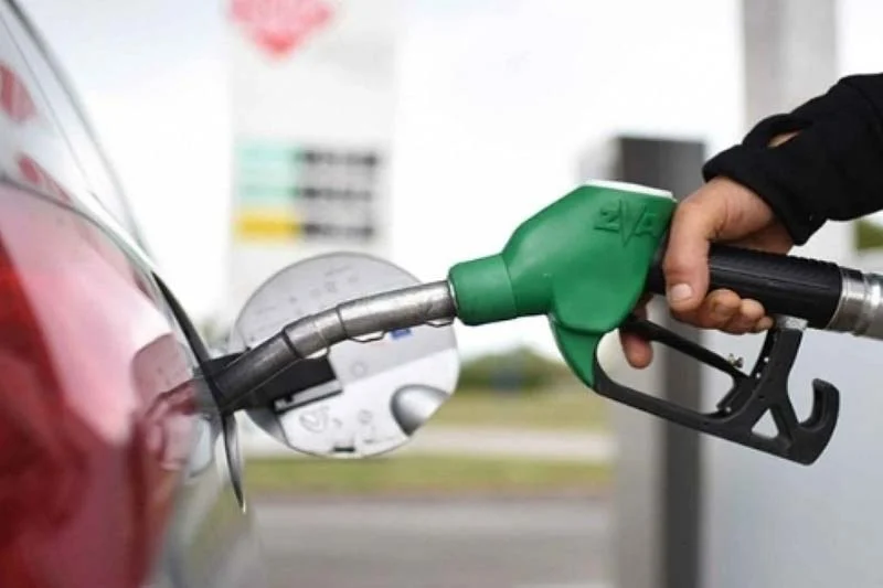 Person pumping gasoline into a red car using a green fuel nozzle at a gas station