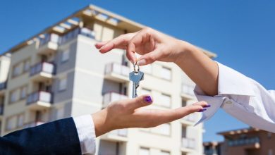 Two people exchanging a keyring in front of a modern apartment building, signaling a rental or purchase handoff.