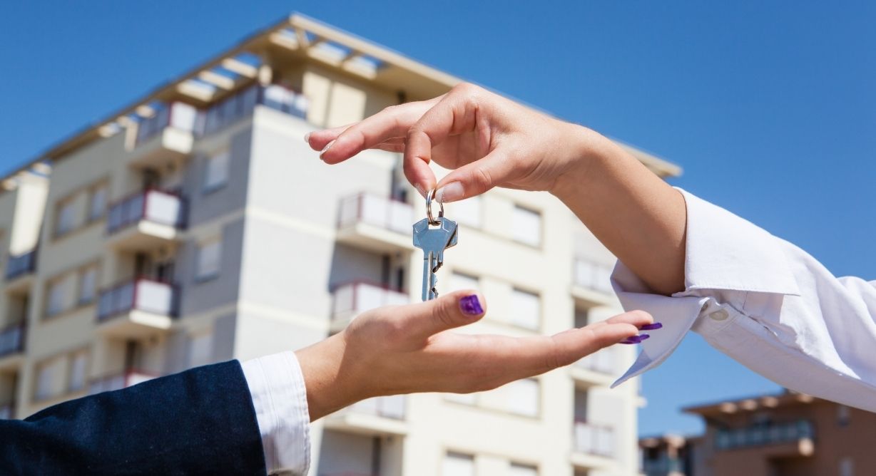 Comment-refaire-une-clé-d-appartement | MCG24 | موقع إلكتروني مغربي شامل متجدد على مدار الساعة Two people exchanging a keyring in front of a modern apartment building, signaling a rental or purchase handoff.