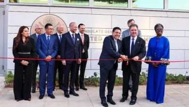 Group of officials standing for a ribbon-cutting ceremony outside a government building, with a red ribbon stretched across the scene.