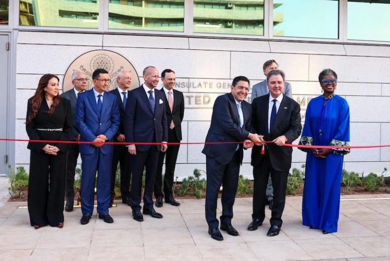 Group of officials standing for a ribbon-cutting ceremony outside a government building, with a red ribbon stretched across the scene.
