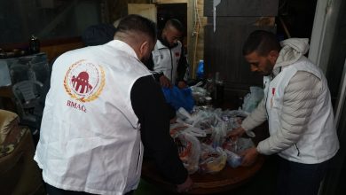 Volunteer group wearing white vests with BMAQ logo sorting donated bags of supplies on a table indoors.