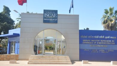 Entrance to Groupe ISCAE building with a blue sign reading 'GROUPE ISCAE' and Arabic text, glass doors, and steps; Moroccan flag on a flagpole to the left.