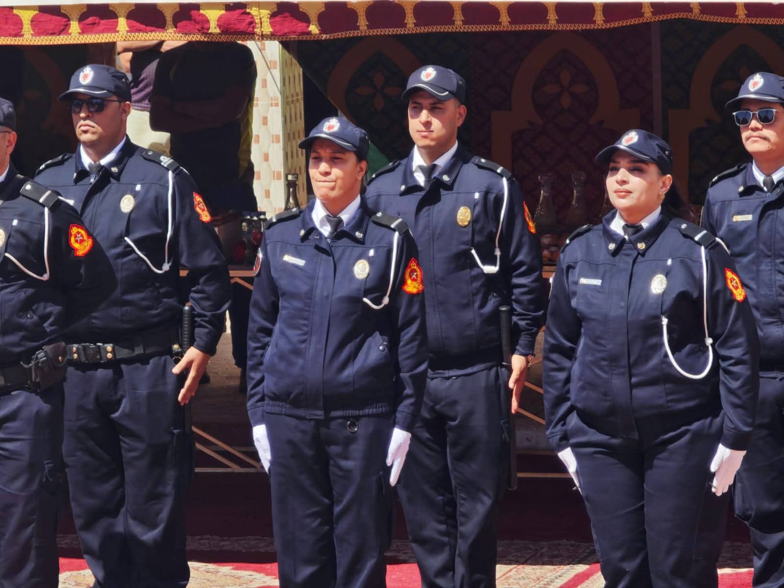 Group of uniformed officers standing in a line at a formal event, wearing navy blue attire and caps with badges.