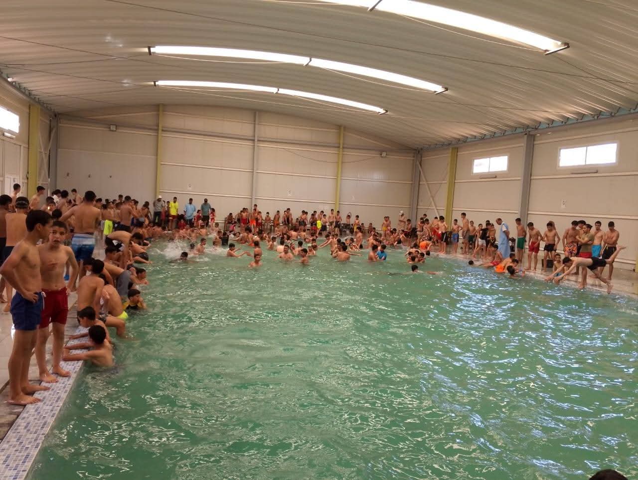 FB_IMG_1779639592554 | MCG24 | موقع إلكتروني مغربي شامل متجدد على مدار الساعة Large indoor swimming pool filled with children and adults along the edges and swimming in the water.