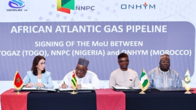 Four officials sign a MoU at a long table with red table runners, flags, and a blue backdrop reading 'AFRICAN ATLANTIC GAS PIPELINE'.