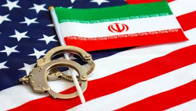 Handcuffs resting on a U.S. flag with a small Iranian flag laid across it, suggesting tension between the two nations.