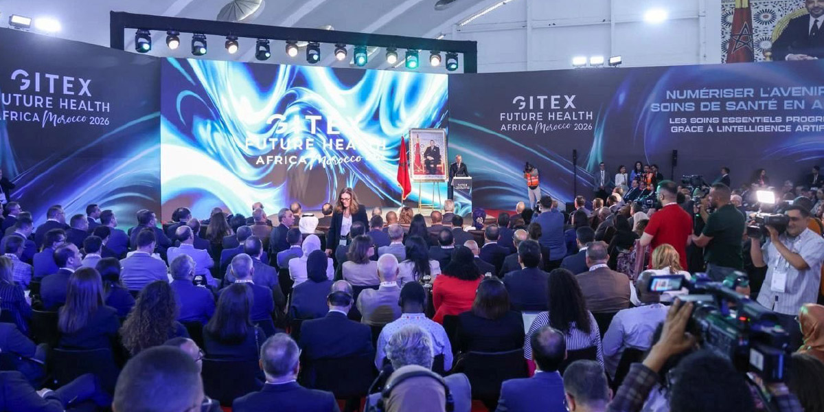 Stage at a large conference with blue, swirling backdrop reading 'GITEX Future Health Africa Morocco 2026' and a seated audience in front of a presenter podium.
