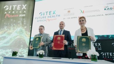 Three professionals on a stage hold red, green, and blue folders during a conference, with GITEX Africa Morocco banners in the background.
