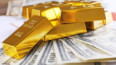 Gold-Dollar | MCG24 | موقع إلكتروني مغربي شامل متجدد على مدار الساعة Gold bullion bars stacked on top of US hundred-dollar bills, symbolizing wealth and investment.