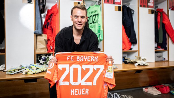 Man in a locker room displaying an orange FC Bayern jersey with 2027 and Neuer printed on it.