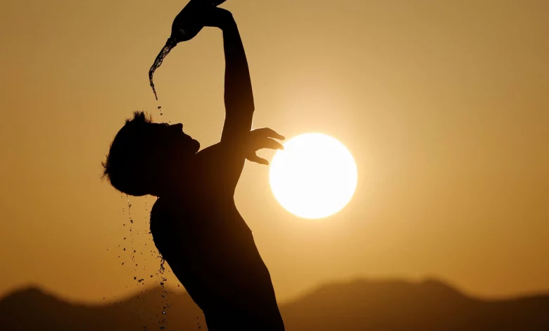 Silhouette of a person tilting a bottle to pour water over their head at sunset.