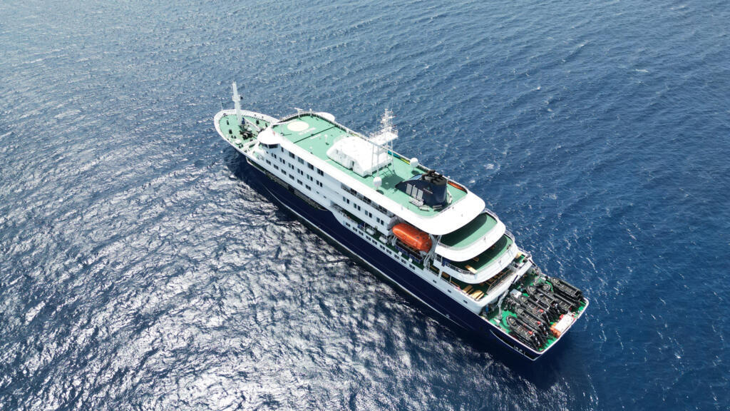 Overhead view of a large cruise ship with multiple decks sailing on deep blue ocean water from above.