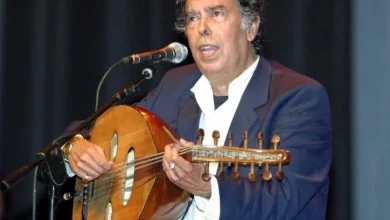 Man in a blue blazer and white shirt playing an oud and singing into a microphone on stage