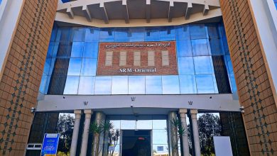 Entrance to SRM Oriental building with brick sign and Arabic script, glass façade, and decorative columns.