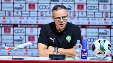 IMG-20260317-WA0024-1024x568 | MCG24 | موقع إلكتروني مغربي شامل متجدد على مدار الساعة Male football official with Morocco crest speaks at a press conference, microphone in front, plus a water bottle, Pepsi can, model airplane, and a football on the table.