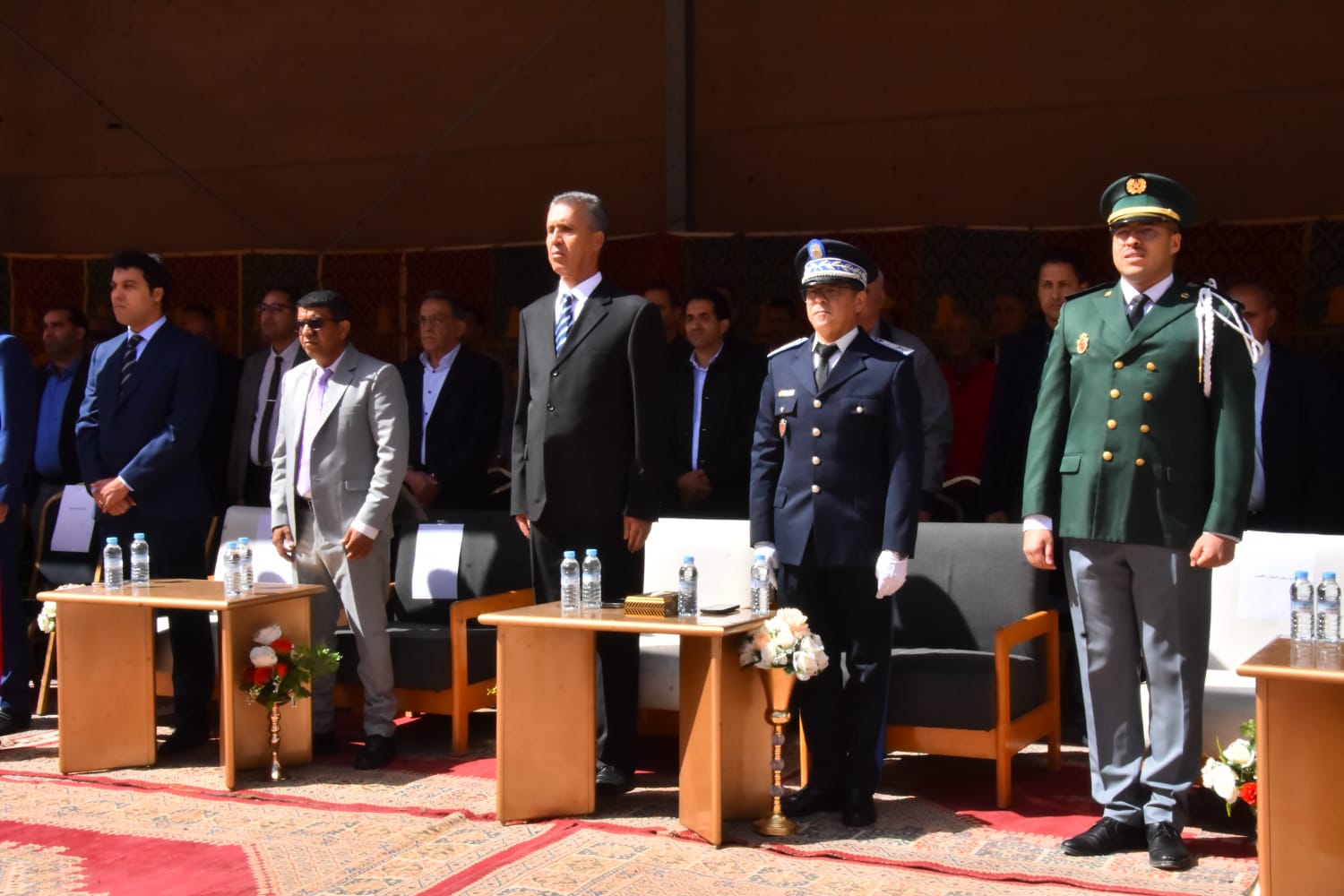 IMG-20260516-WA0017 | MCG24 | موقع إلكتروني مغربي شامل متجدد على مدار الساعة Group of formally dressed officials and uniformed officers standing at a ceremony, with tables and water bottles in front of them